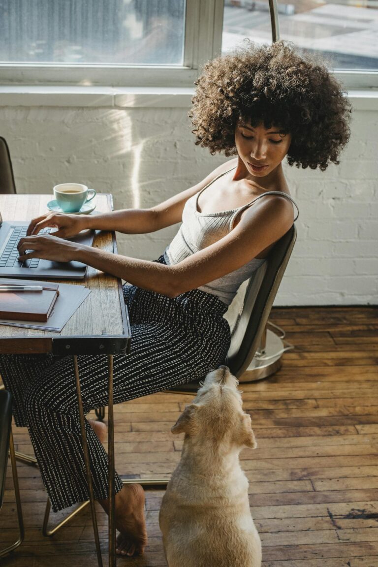 Young woman working from home on a laptop with her dog, embodying modern freelance lifestyle.